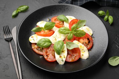 Photo of Tasty salad Caprese with mozzarella, tomatoes, basil and spices on black table, closeup