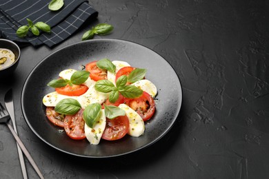 Photo of Tasty salad Caprese with mozzarella, tomatoes, basil and spices on black table, closeup. Space for text