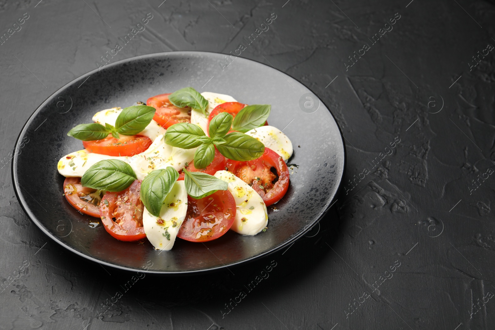 Tasty salad Caprese with mozzarella, tomatoes, basil and spices on black table, closeup. Space for text Photo of Tasty salad Caprese with mozzarella, tomatoes, basil and spices on black table, closeup. Space for text