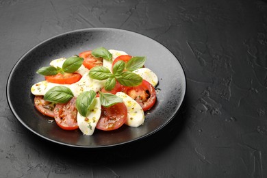 Photo of Tasty salad Caprese with mozzarella, tomatoes, basil and spices on black table, closeup. Space for text
