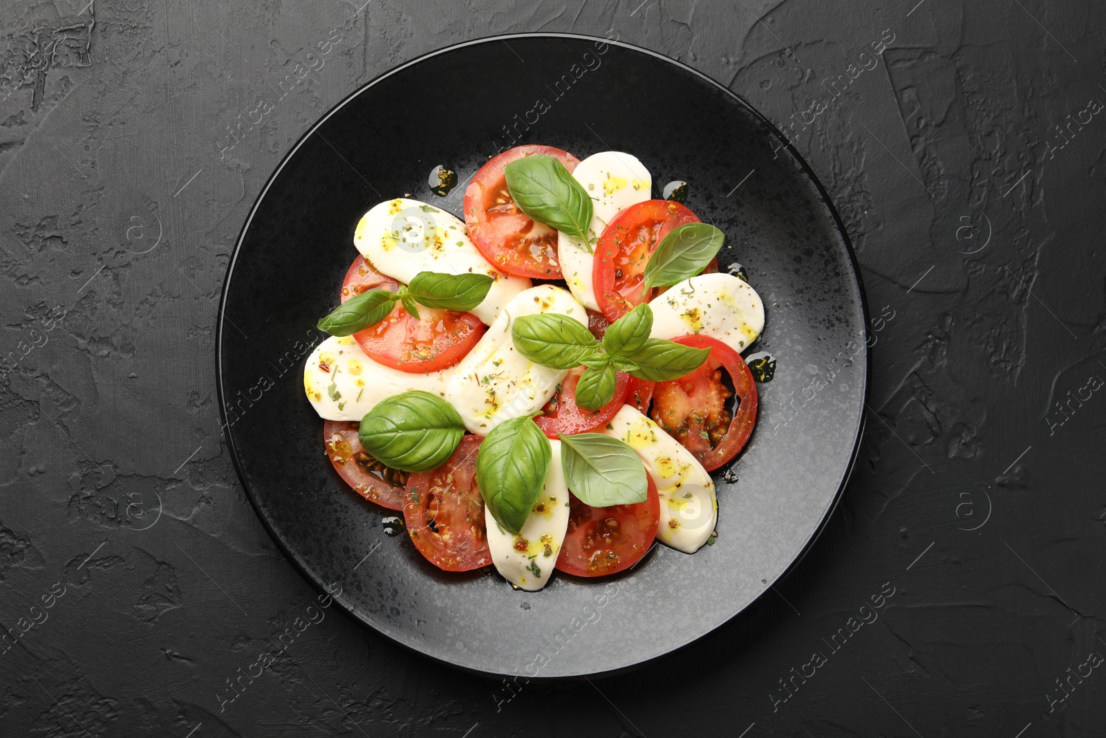 Tasty salad Caprese with mozzarella, tomatoes, basil and spices on black table, top view Photo of Tasty salad Caprese with mozzarella, tomatoes, basil and spices on black table, top view