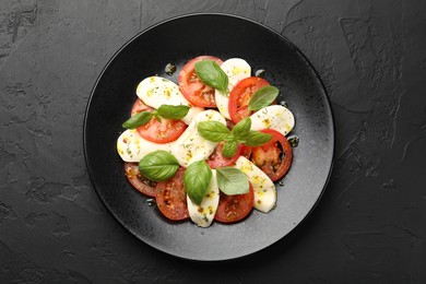 Photo of Tasty salad Caprese with mozzarella, tomatoes, basil and spices on black table, top view