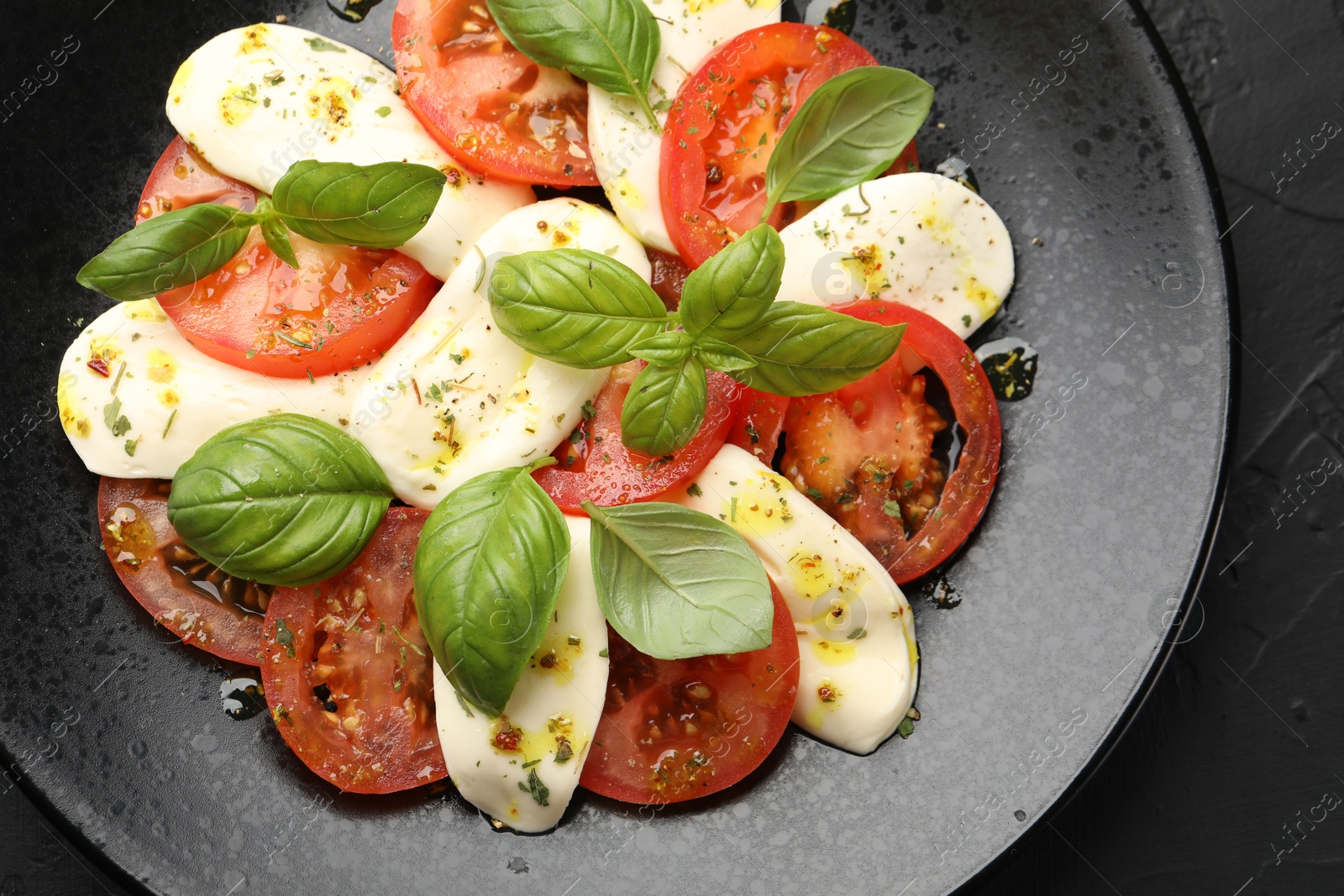 Tasty salad Caprese with mozzarella, tomatoes, basil and spices on black table, top view Photo of Tasty salad Caprese with mozzarella, tomatoes, basil and spices on black table, top view