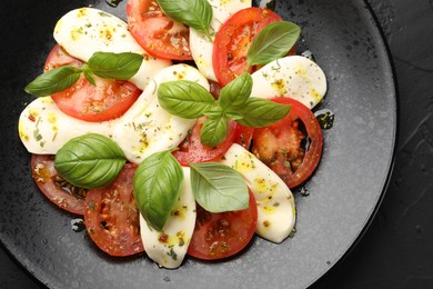Photo of Tasty salad Caprese with mozzarella, tomatoes, basil and spices on black table, top view