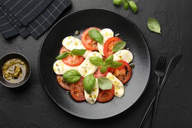 Photo of Tasty salad Caprese with mozzarella, tomatoes, basil and spices on black table, flat lay