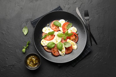 Photo of Tasty salad Caprese with mozzarella, tomatoes, basil and spices on black table, flat lay