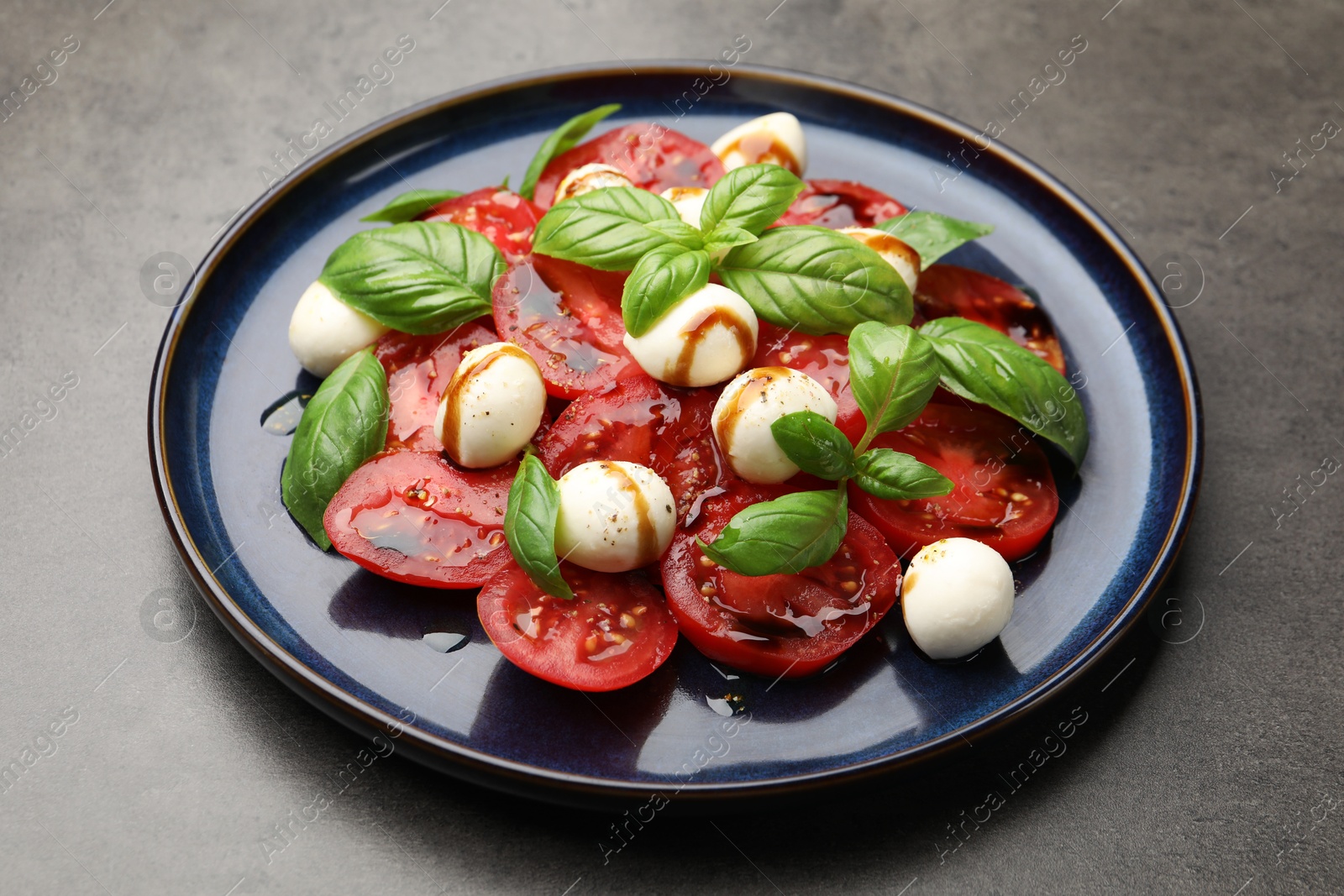 Tasty salad Caprese with mozzarella, tomatoes, basil and balsamic vinegar on grey table, closeup Photo of Tasty salad Caprese with mozzarella, tomatoes, basil and balsamic vinegar on grey table, closeup