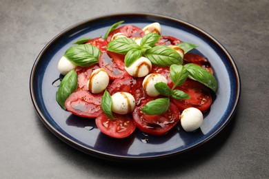 Photo of Tasty salad Caprese with mozzarella, tomatoes, basil and balsamic vinegar on grey table, closeup
