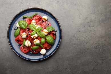 Photo of Tasty salad Caprese with mozzarella, tomatoes, basil and balsamic vinegar on grey table, top view. Space for text