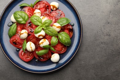 Photo of Tasty salad Caprese with mozzarella, tomatoes, basil and balsamic vinegar on grey table, top view. Space for text