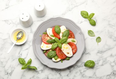Photo of Tasty salad Caprese with mozzarella, tomatoes, basil and spices on white marble table, flat lay