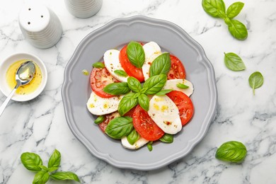 Photo of Tasty salad Caprese with mozzarella, tomatoes, basil and spices on white marble table, flat lay