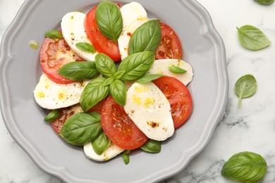 Photo of Tasty salad Caprese with mozzarella, tomatoes, basil and spices on white marble table, flat lay