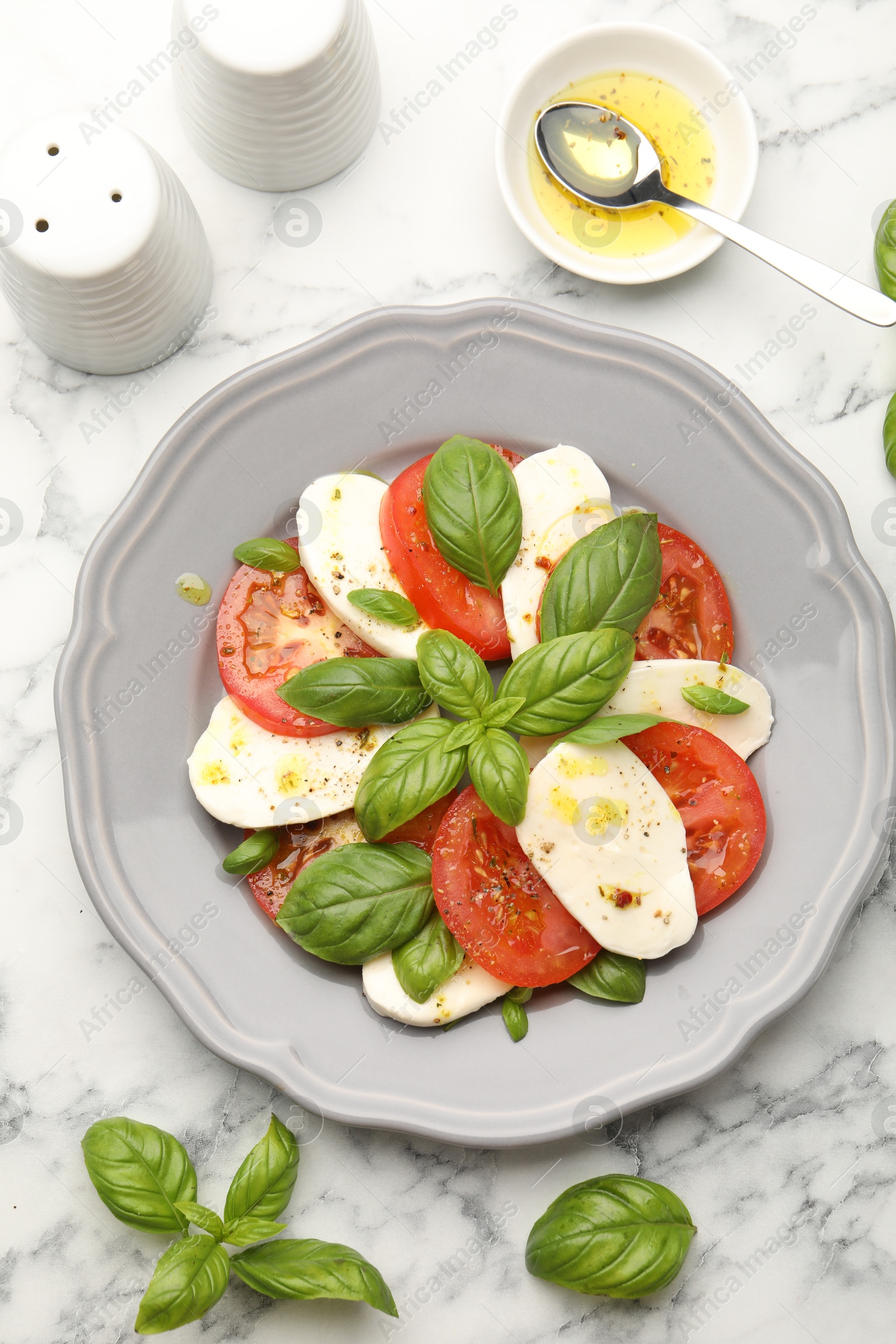 Tasty salad Caprese with mozzarella, tomatoes, basil and spices on white marble table, flat lay Photo of Tasty salad Caprese with mozzarella, tomatoes, basil and spices on white marble table, flat lay