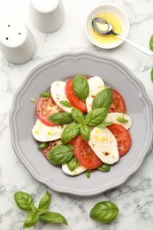 Photo of Tasty salad Caprese with mozzarella, tomatoes, basil and spices on white marble table, flat lay