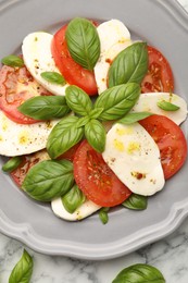 Photo of Tasty salad Caprese with mozzarella, tomatoes, basil and spices on white marble table, top view
