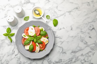 Photo of Tasty salad Caprese with mozzarella, tomatoes, basil and spices on white marble table, flat lay. Space for text