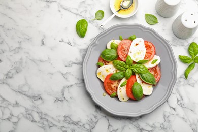 Photo of Tasty salad Caprese with mozzarella, tomatoes, basil and spices on white marble table, flat lay. Space for text
