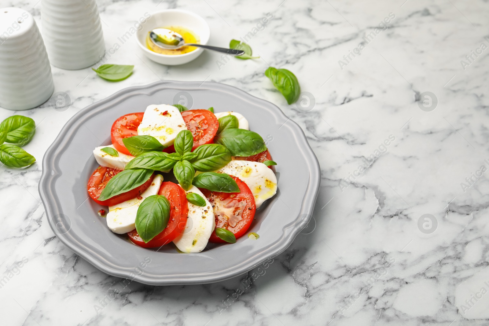 Tasty salad Caprese with mozzarella, tomatoes, basil and spices on white marble table, closeup. Space for text Photo of Tasty salad Caprese with mozzarella, tomatoes, basil and spices on white marble table, closeup. Space for text