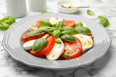 Photo of Tasty salad Caprese with mozzarella, tomatoes, basil and spices on white marble table, closeup