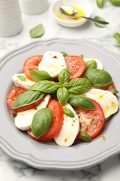Photo of Tasty salad Caprese with mozzarella, tomatoes, basil and spices on white marble table, closeup