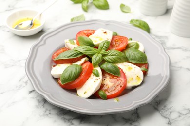 Photo of Tasty salad Caprese with mozzarella, tomatoes, basil and spices on white marble table, closeup