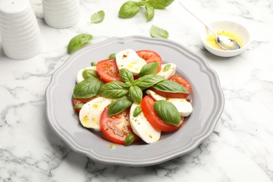Photo of Tasty salad Caprese with mozzarella, tomatoes, basil and spices on white marble table, closeup