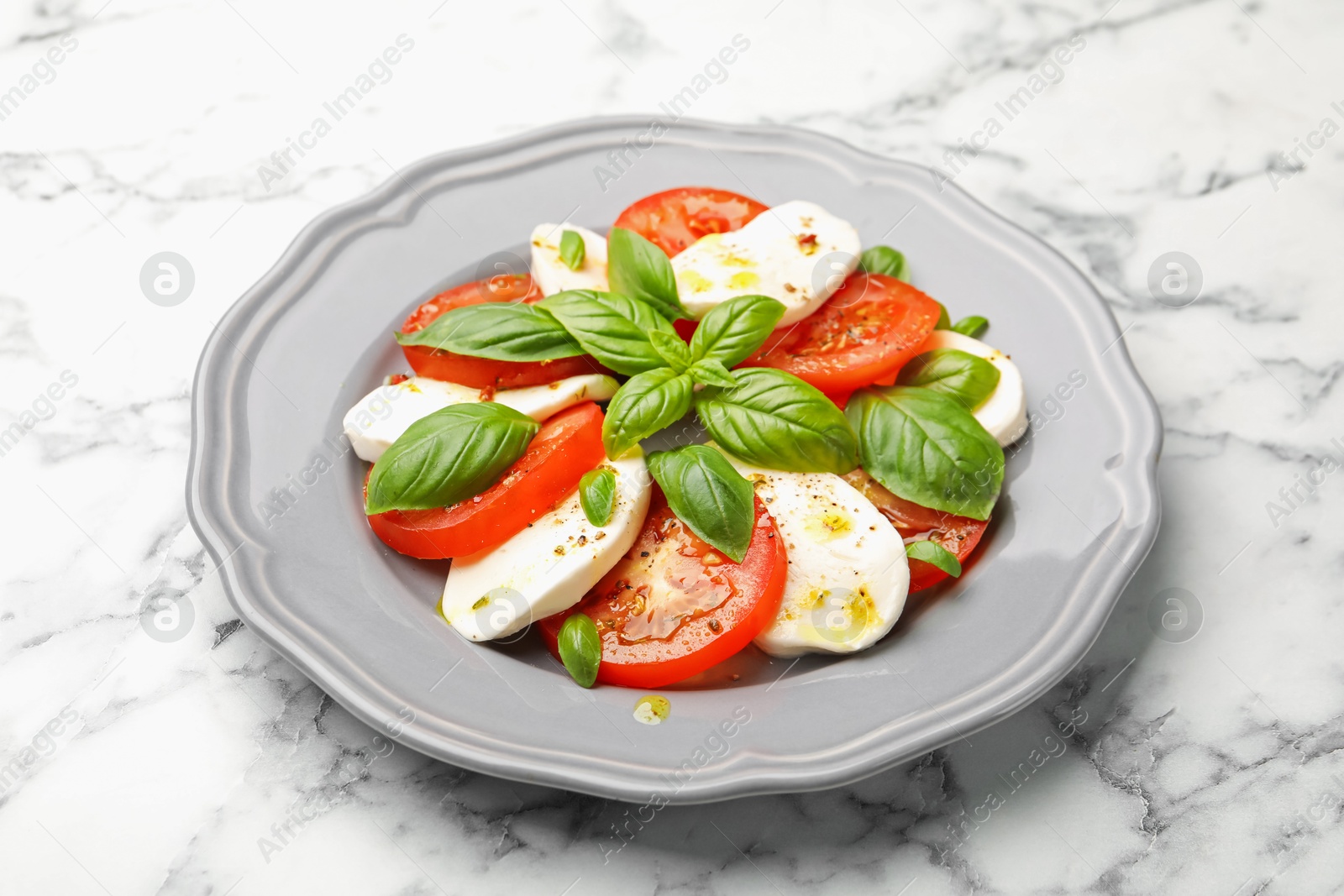 Tasty salad Caprese with mozzarella, tomatoes, basil and spices on white marble table, closeup Photo of Tasty salad Caprese with mozzarella, tomatoes, basil and spices on white marble table, closeup