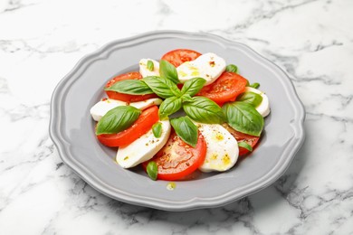 Photo of Tasty salad Caprese with mozzarella, tomatoes, basil and spices on white marble table, closeup