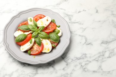 Photo of Tasty salad Caprese with mozzarella, tomatoes, basil and spices on white marble table, above view. Space for text