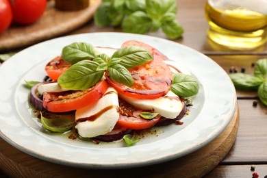 Photo of Tasty salad Caprese with mozzarella, tomatoes, basil and spices on wooden table, closeup