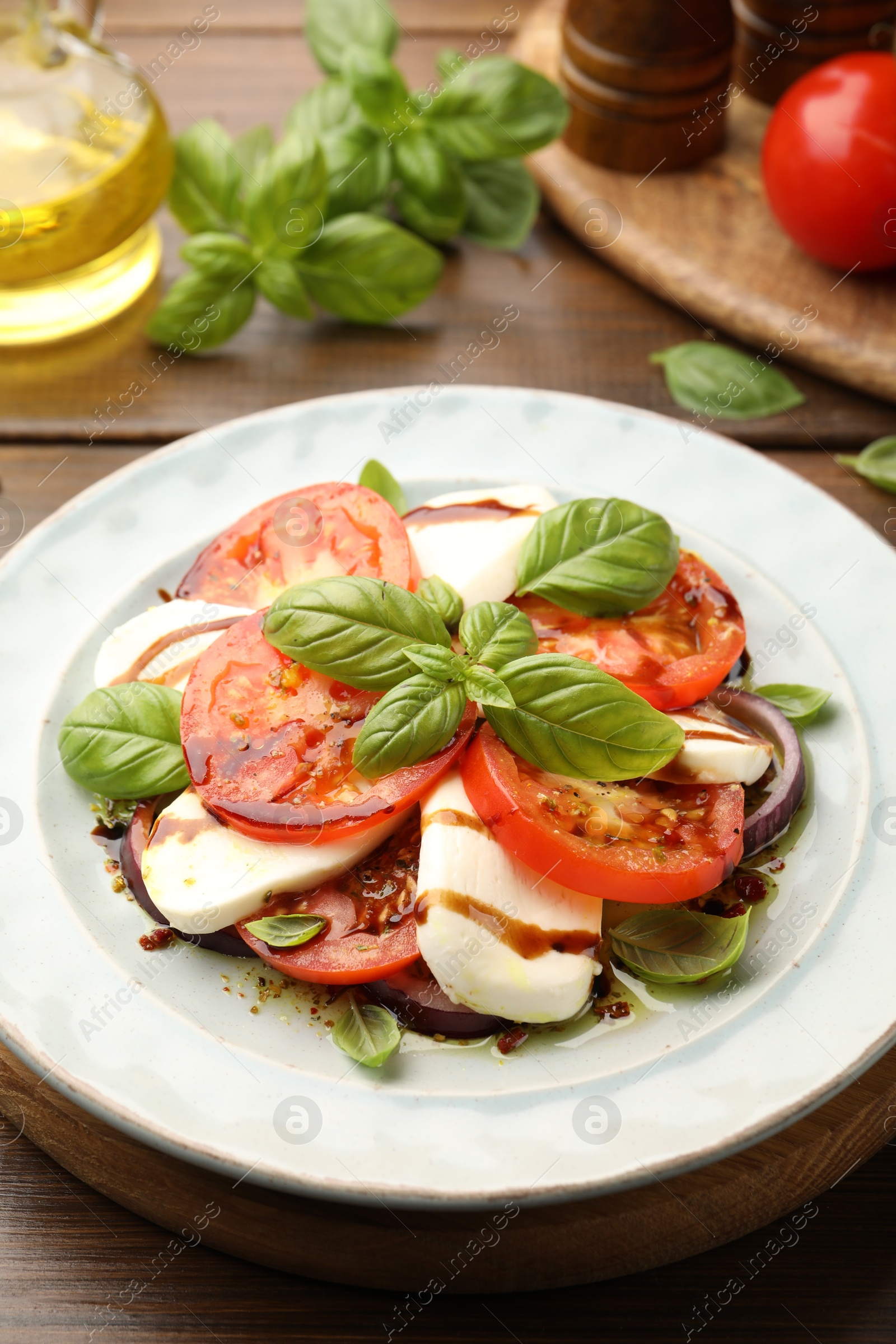 Tasty salad Caprese with mozzarella, tomatoes, basil and spices on wooden table, closeup Photo of Tasty salad Caprese with mozzarella, tomatoes, basil and spices on wooden table, closeup