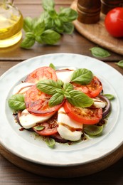 Photo of Tasty salad Caprese with mozzarella, tomatoes, basil and spices on wooden table, closeup