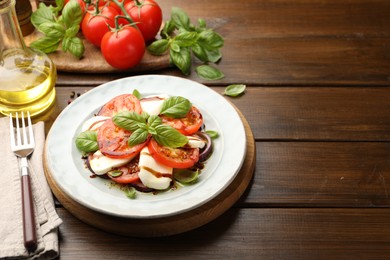 Photo of Tasty salad Caprese with mozzarella, tomatoes, basil and spices on wooden table, closeup. Space for text