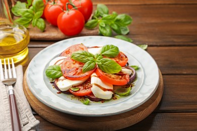 Photo of Tasty salad Caprese with mozzarella, tomatoes, basil and spices on wooden table, closeup