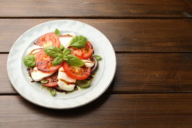 Photo of Tasty salad Caprese with mozzarella, tomatoes, basil and spices on wooden table, space for text