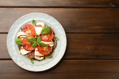 Photo of Tasty salad Caprese with mozzarella, tomatoes, basil and spices on wooden table, top view. Space for text