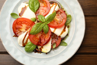 Photo of Tasty salad Caprese with mozzarella, tomatoes, basil and spices on wooden table, top view