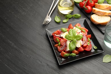 Photo of Tasty salad Caprese served on black table, above view. Space for text