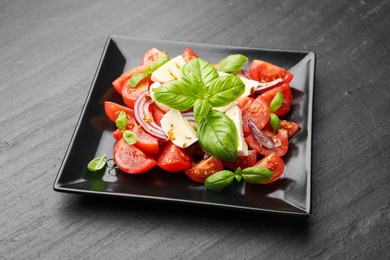 Photo of Tasty salad Caprese with mozzarella, tomatoes, basil, onion and spices on black table, closeup