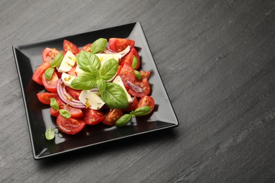 Photo of Tasty salad Caprese with mozzarella, tomatoes, basil, onion and spices on black table, above view. Space for text