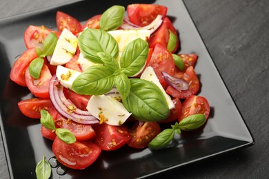 Photo of Tasty salad Caprese with mozzarella, tomatoes, basil, onion and spices on black table, closeup