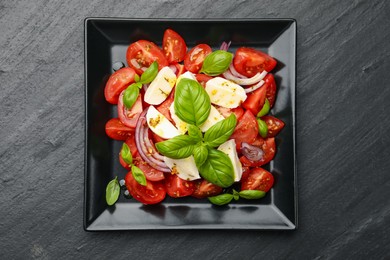 Photo of Tasty salad Caprese with mozzarella, tomatoes, basil, onion and spices on black table, top view