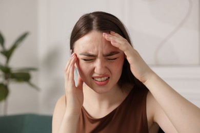 Photo of Young woman suffering from headache at home