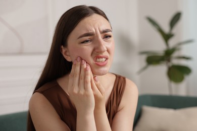 Photo of Young woman suffering from toothache at home
