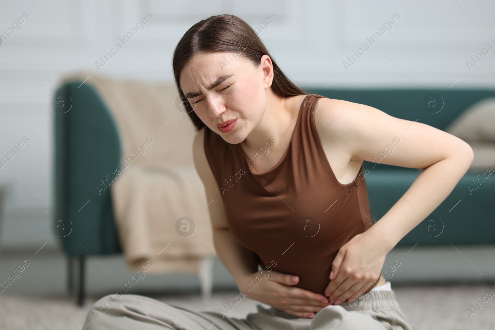 Woman suffering from abdominal pain on floor at home, space for text Photo of Woman suffering from abdominal pain on floor at home, space for text