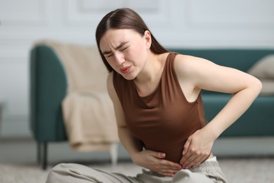 Photo of Woman suffering from abdominal pain on floor at home, space for text