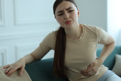 Photo of Woman suffering from abdominal pain on sofa at home