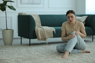 Photo of Woman suffering from knee pain on floor at home, space for text