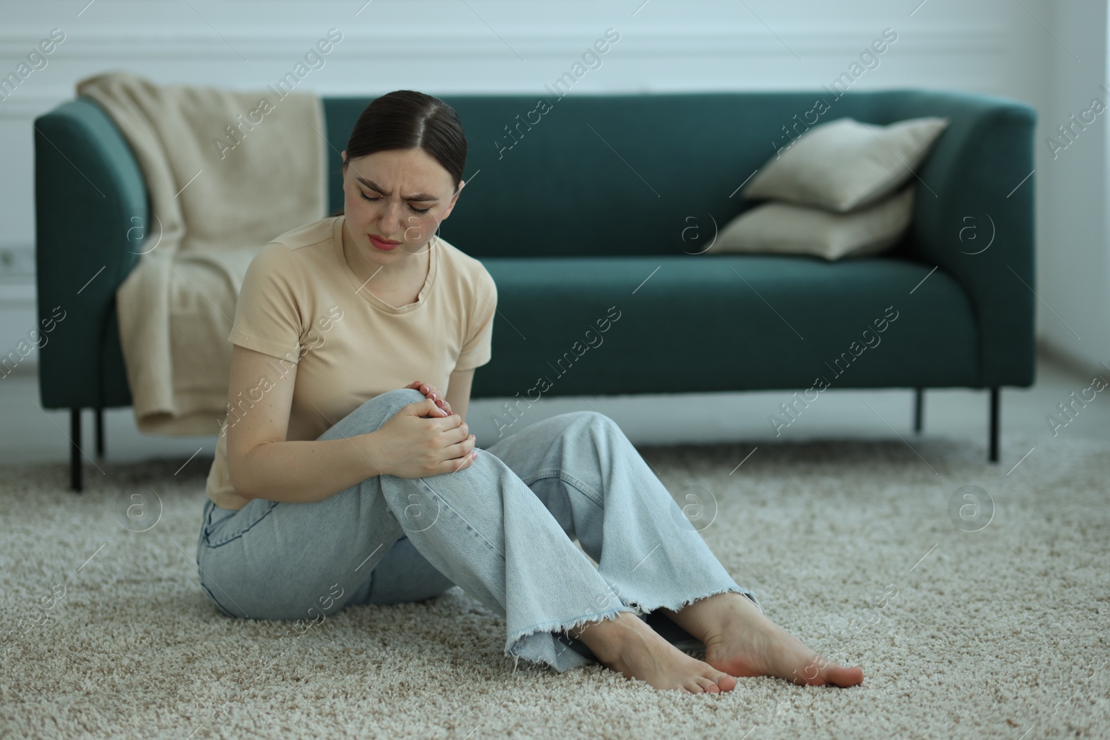 Woman suffering from knee pain on floor at home Photo of Woman suffering from knee pain on floor at home